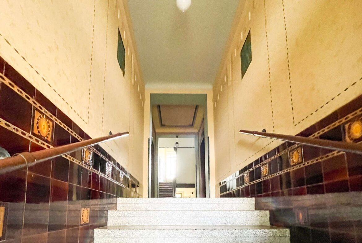Long view of a tiled stairwell with brown glossy wall tiles and decorative round inserts, converging to a doorway at the top.