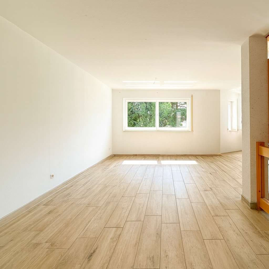 Empty bright living room with light wood flooring and a large window letting in natural light