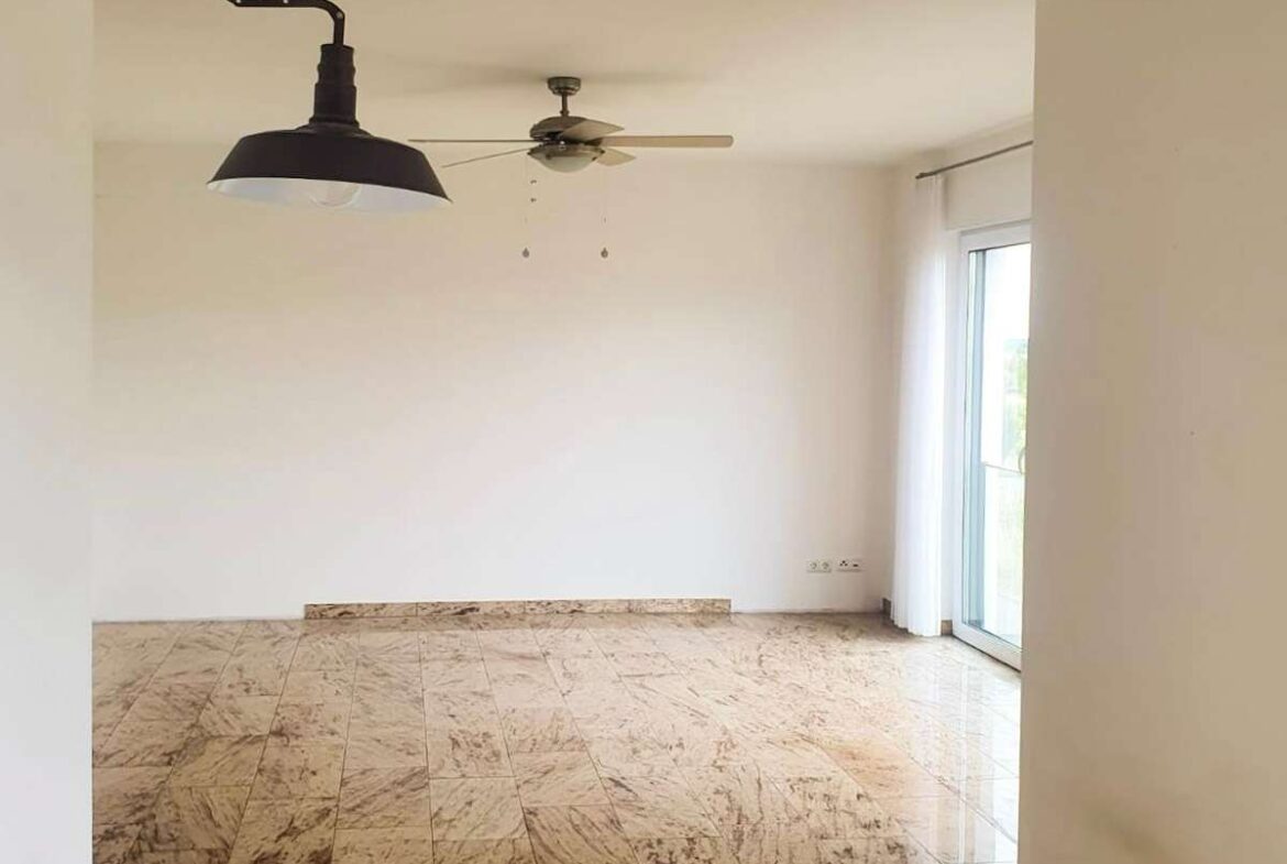 Empty living room with marble tile floor, white walls, a ceiling fan, and a black pendant light, plus glass doors with sheer curtains.