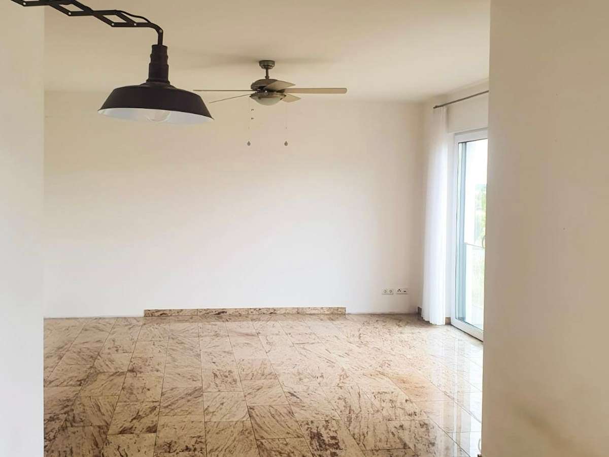 Empty living room with marble tile floor, white walls, a ceiling fan, and a black pendant light, plus glass doors with sheer curtains.