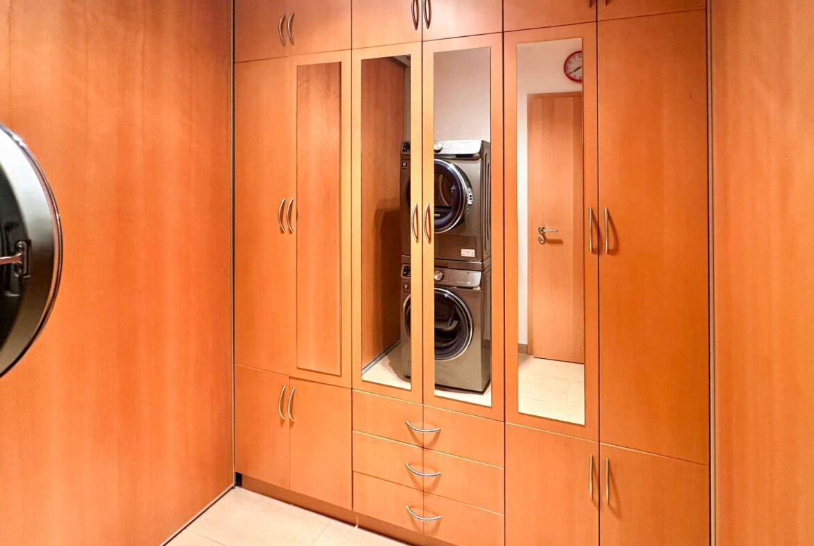 Wooden built-in closet system with mirrored doors; a stacked front-loading washer and dryer visible in the center.