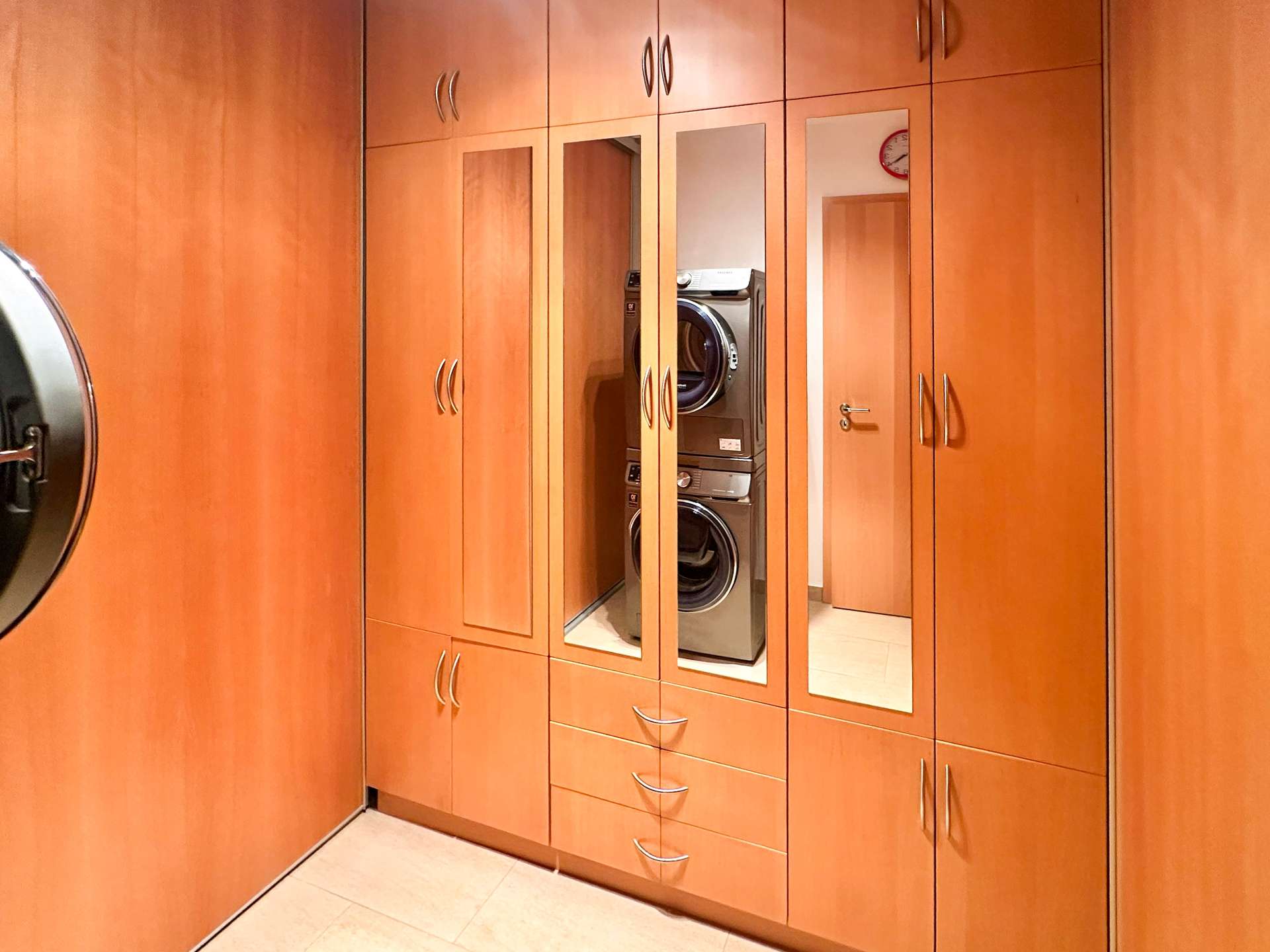 Wooden built-in closet system with mirrored doors; a stacked front-loading washer and dryer visible in the center.