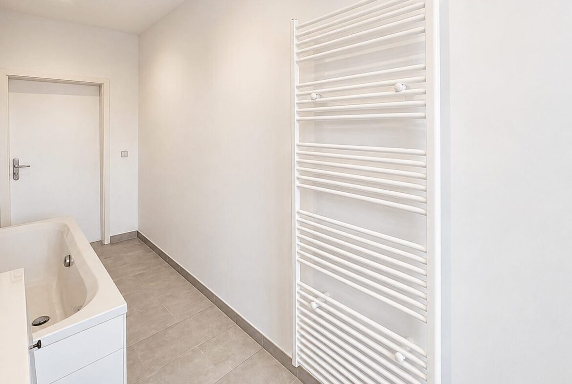 Bright white bathroom with a wall-mounted towel warmer, a white vanity with sink, gray floor tiles, and a closed door.