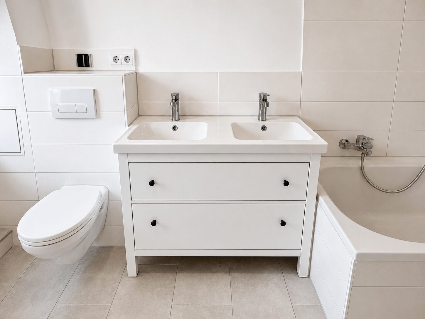 Modern white bathroom with a double-sink vanity, wall-mounted toilet, and a bathtub with chrome fixtures.