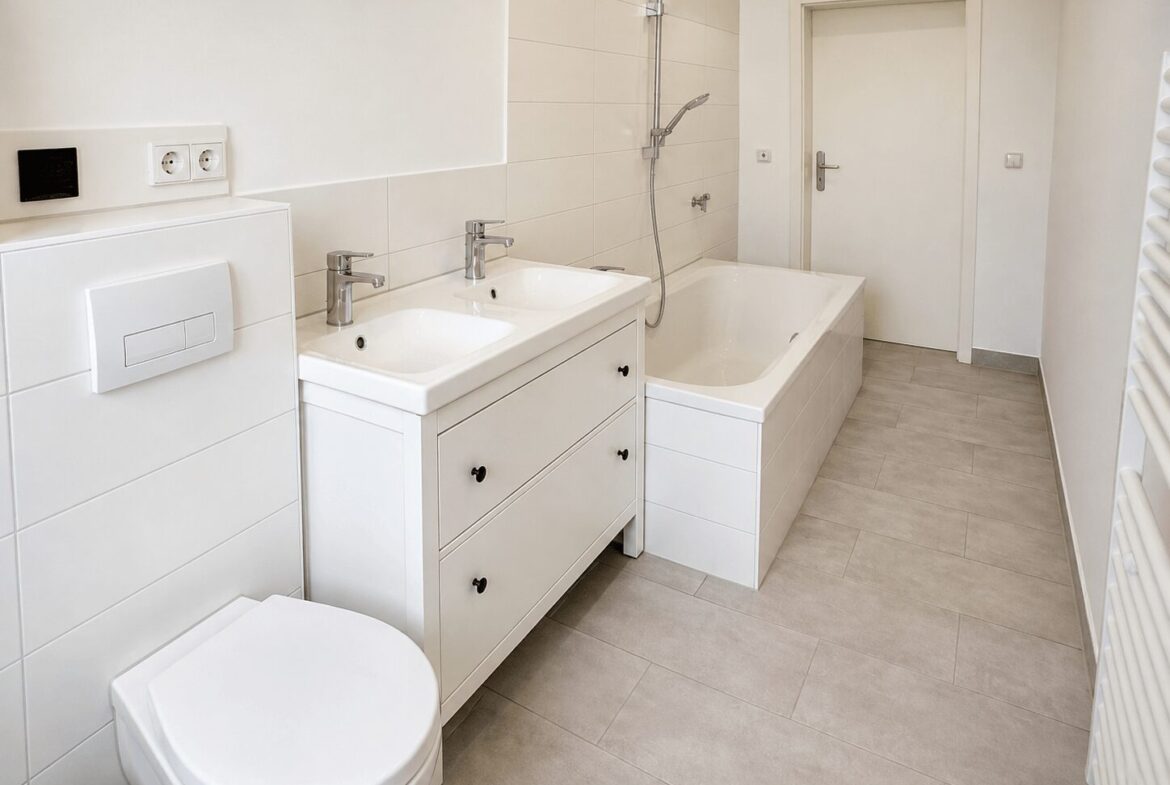 Bright white bathroom with a double sink vanity, a built-in bathtub, and a wall-mounted toilet.