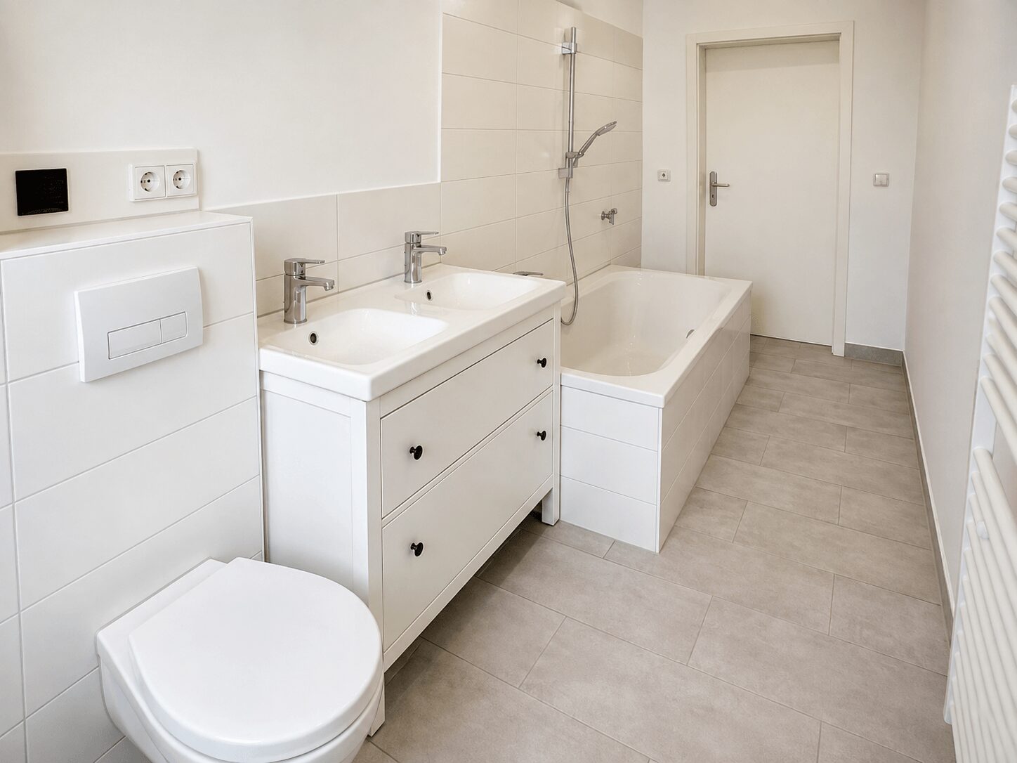 Bright white bathroom with a double sink vanity, a built-in bathtub, and a wall-mounted toilet.