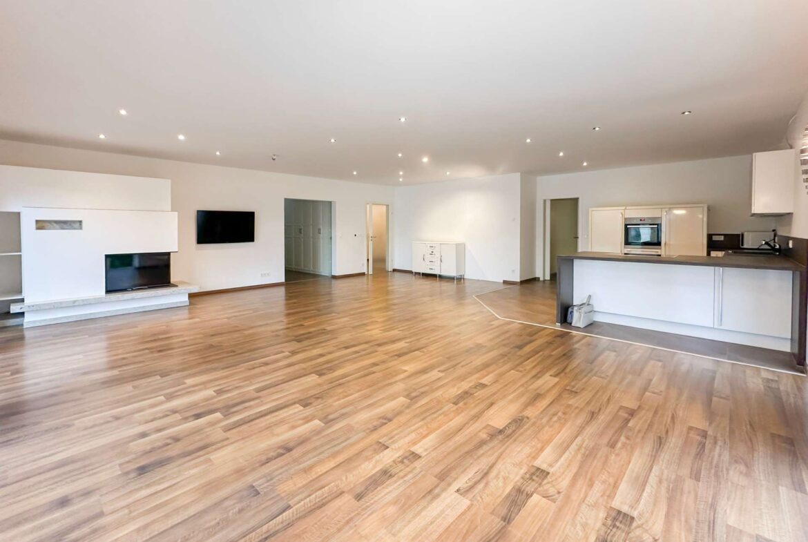 Spacious open-plan living area with hardwood floors, white walls, and a modern kitchen on the right.