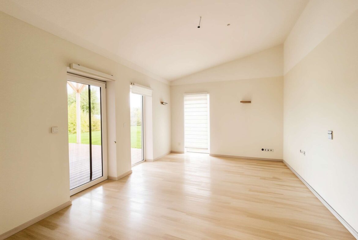 Bright empty living room with light wood floors, beige walls, and sliding glass doors to a Patio/Yard area