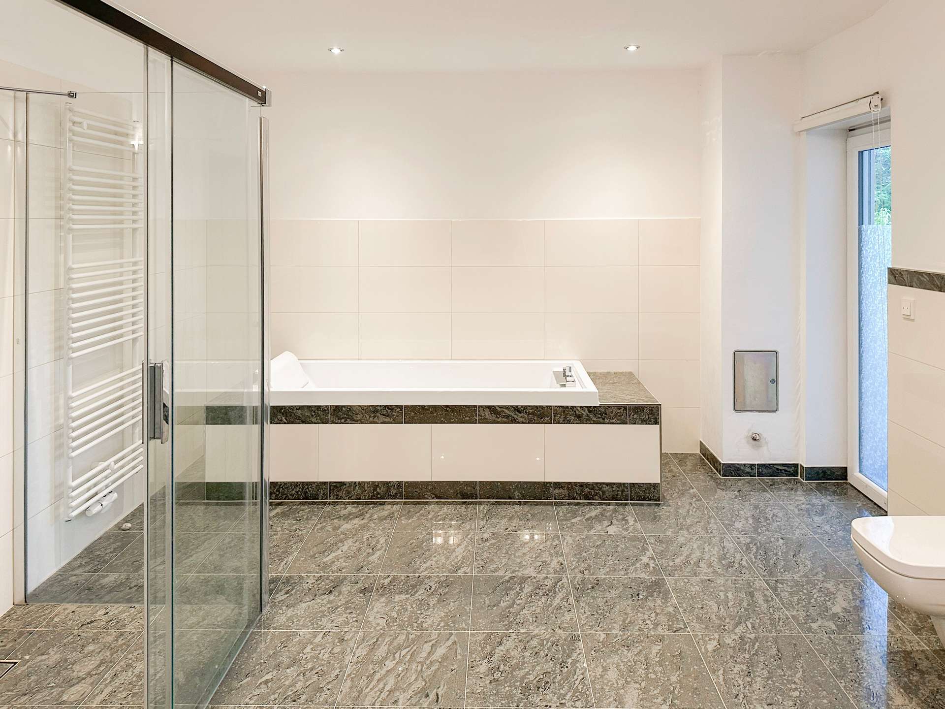 Modern bathroom with a built-in tub along a tiled wall, glass shower enclosure on the left, and a window on the right.