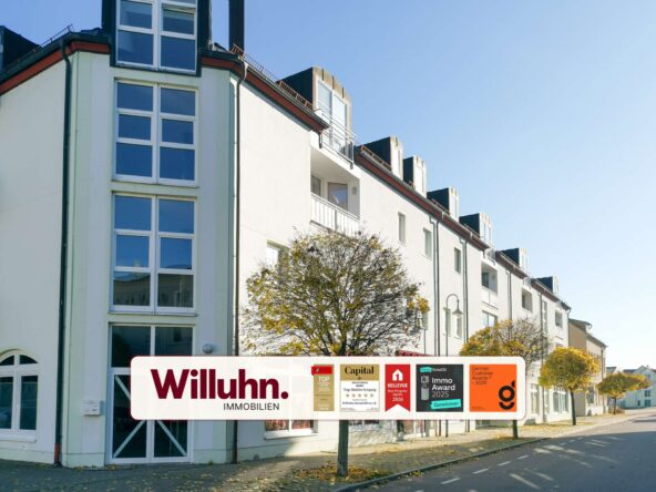 Facade of a white apartment building with a large Willuhn Immobilien banner and award logos along the sidewalk.