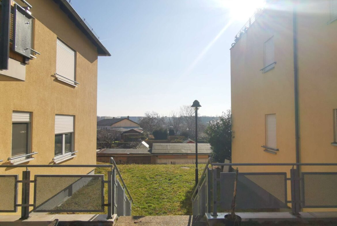Two yellow apartment buildings flank a sunlit courtyard with metal railings and gates, blue sky above.