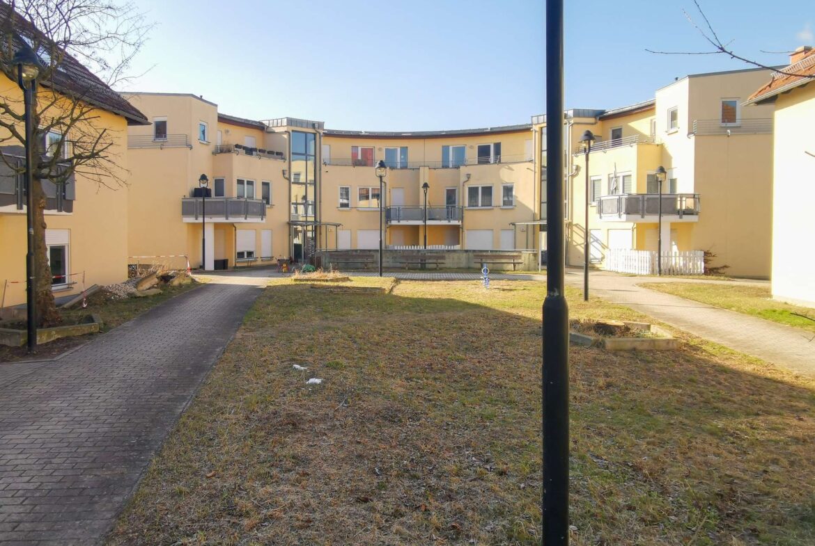 Courtyard of a yellow apartment complex with balconies, curved building, and a central black lamppost against a blue sky