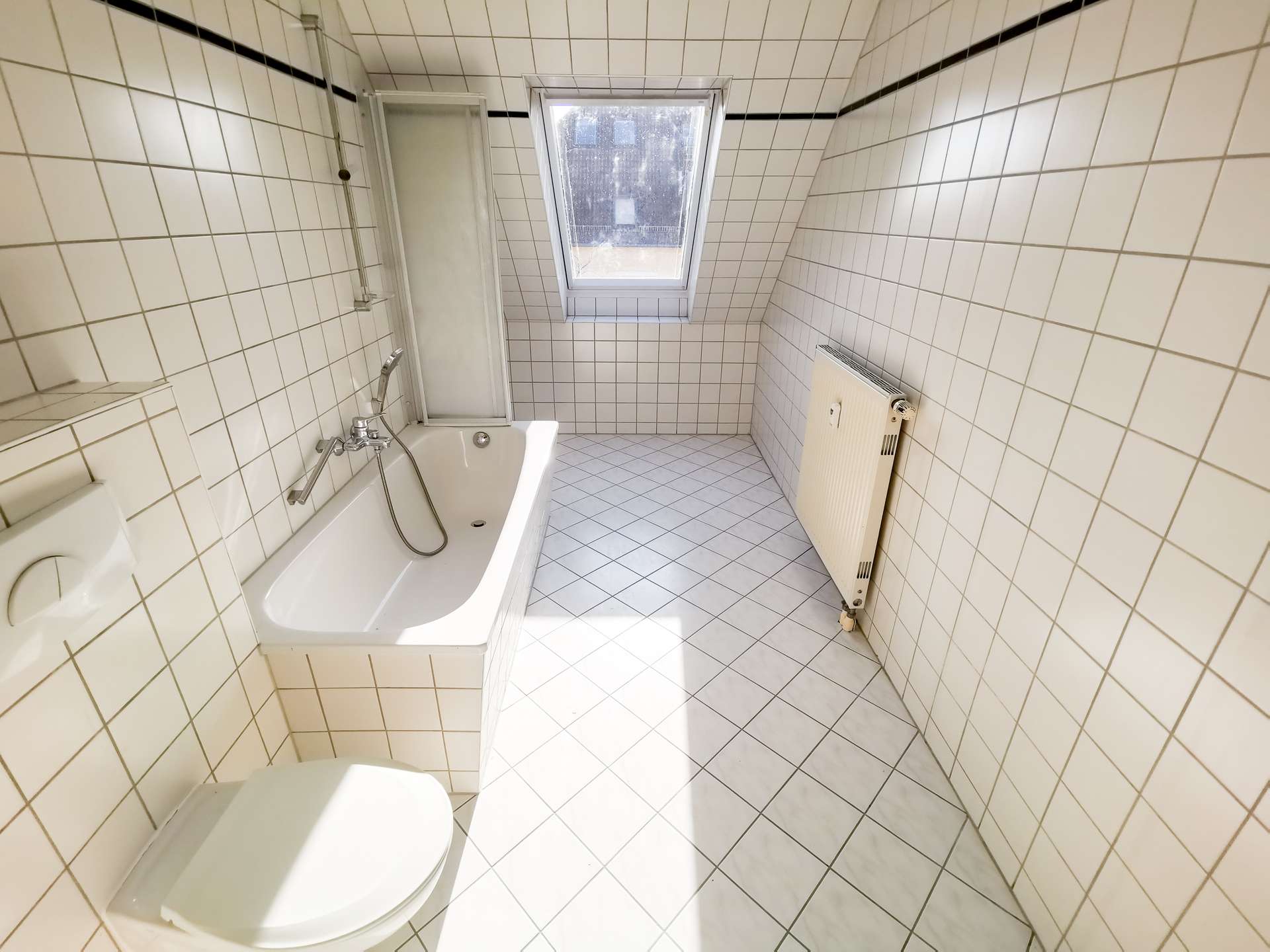Small tiled bathroom with bathtub, shower panel, window, and wall heater.