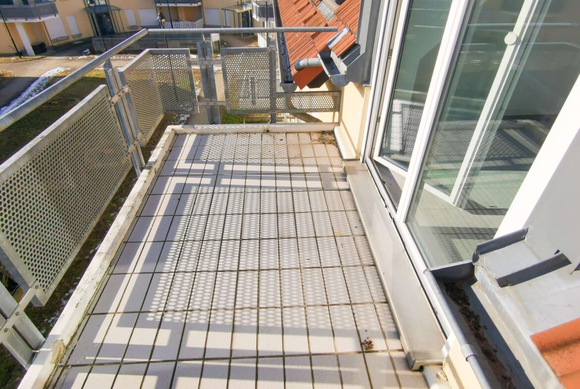 Perspective from a narrow metal-grid balcony looking toward neighboring apartment buildings across a courtyard.