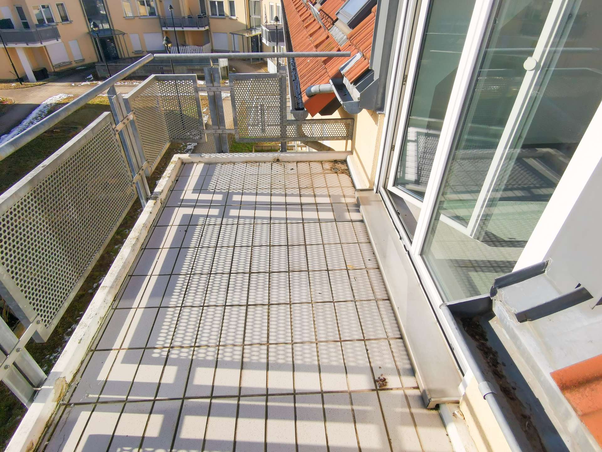 Perspective from a narrow metal-grid balcony looking toward neighboring apartment buildings across a courtyard.