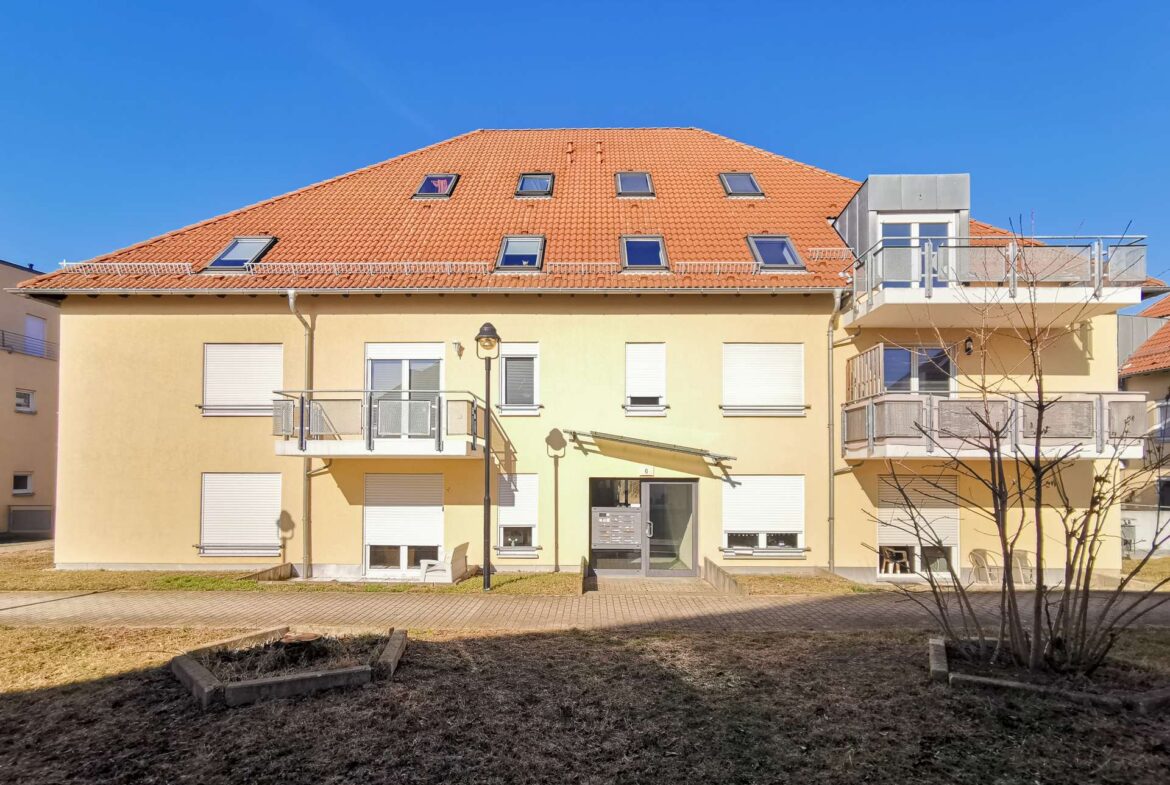 Apartment building with a red-tiled roof and multiple skylights, beige facade, and balconies against a clear blue sky.