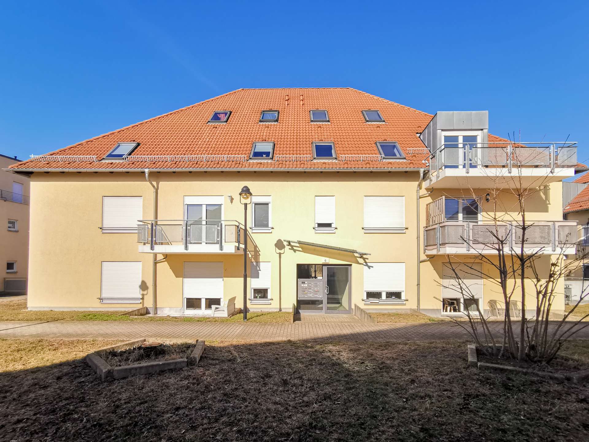 Apartment building with a red-tiled roof and multiple skylights, beige facade, and balconies against a clear blue sky.