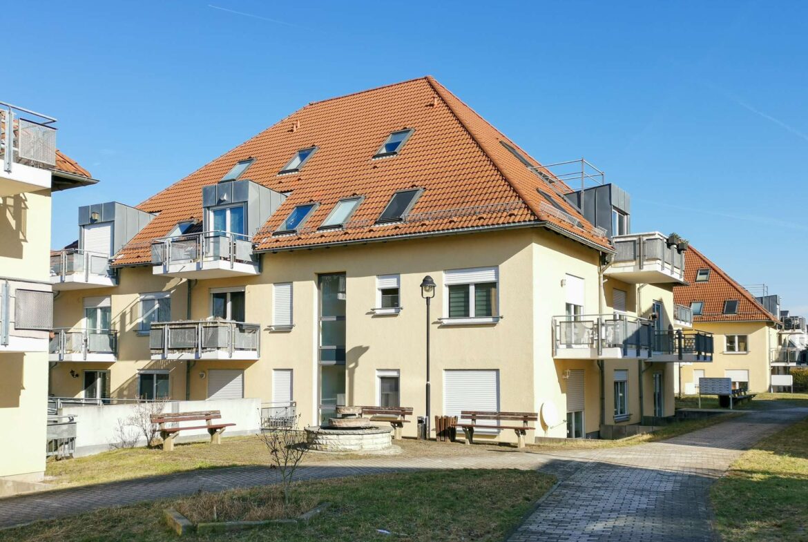 Residential apartment building with yellow walls, red tile pitched roof, and balconies under a clear blue sky