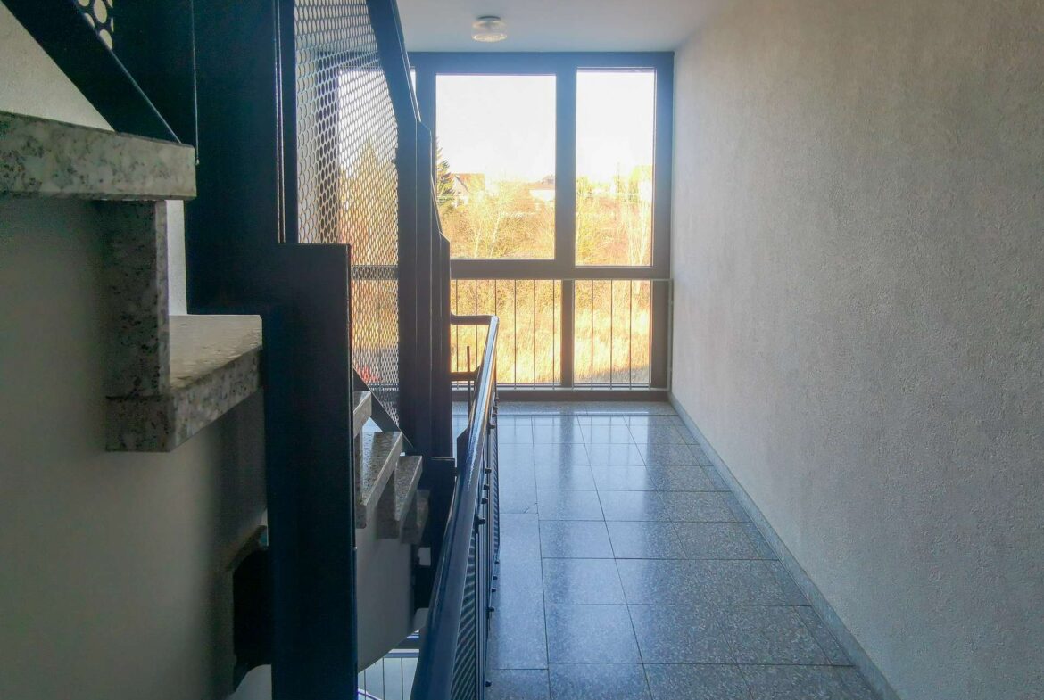 Interior stairwell with dark metal railing and a large window at the end letting in daylight from outside.