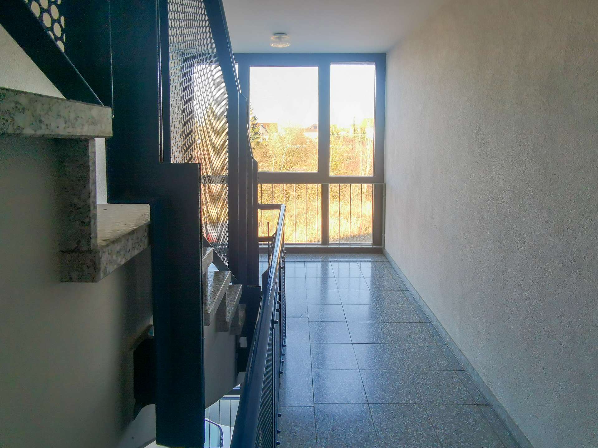 Interior stairwell with dark metal railing and a large window at the end letting in daylight from outside.