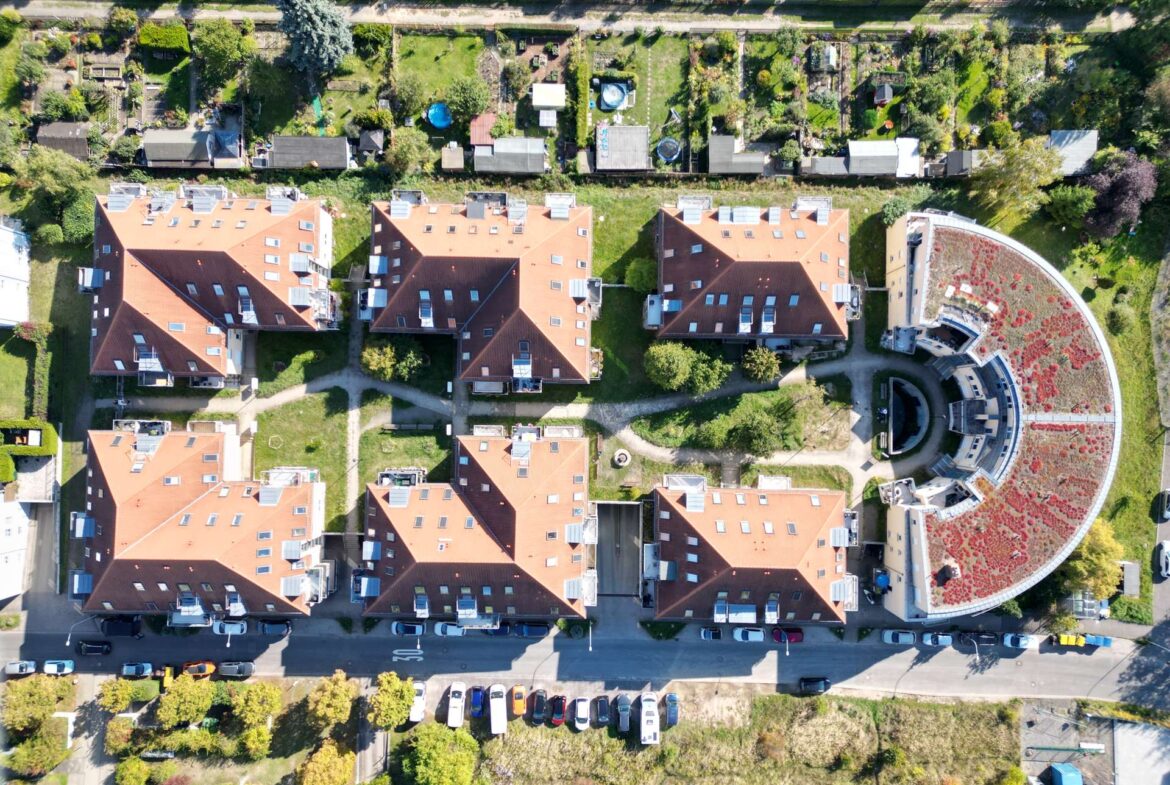 Aerial view of a residential neighborhood with red-roofed apartment buildings and a circular courtyard garden on the right.
