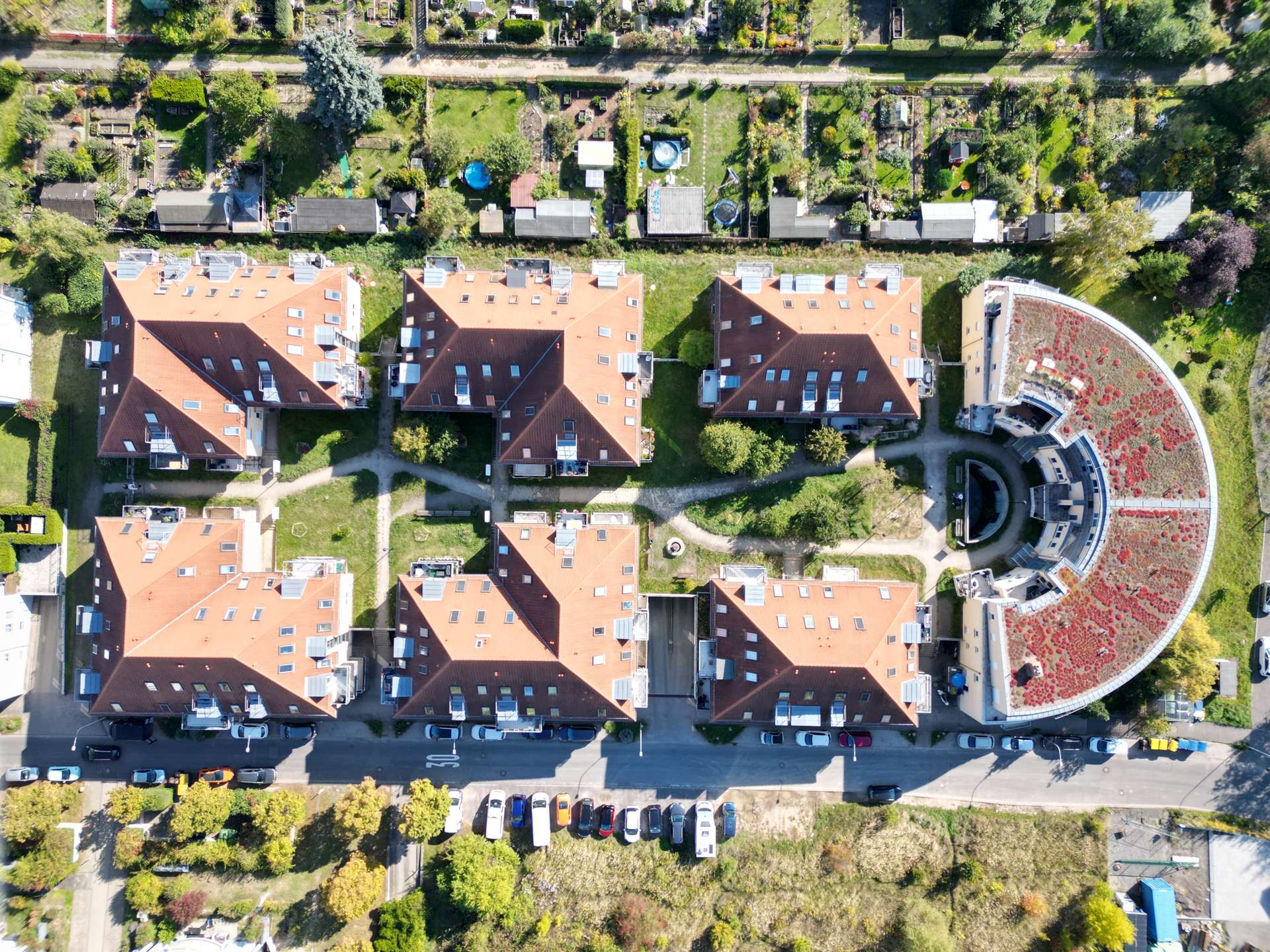 Aerial view of a residential neighborhood with red-roofed apartment buildings and a circular courtyard garden on the right.