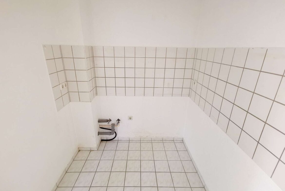 Bare utility corner with white tiled walls, exposed pipes and plumbing under a missing sink area.