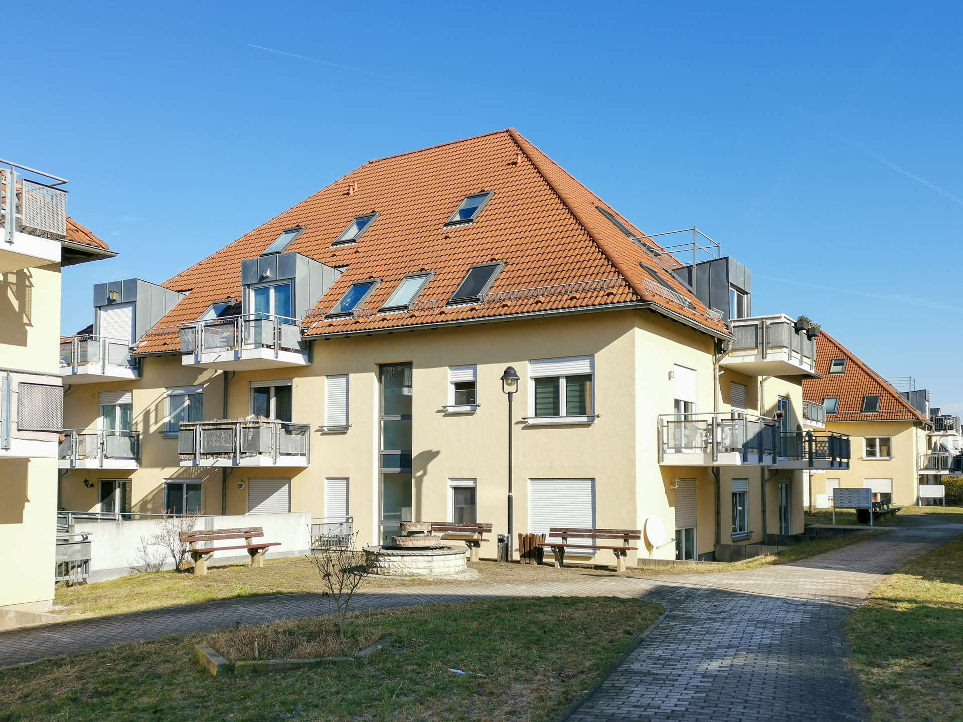 Apartment building with orange tile roof and multiple balconies under a clear blue sky.