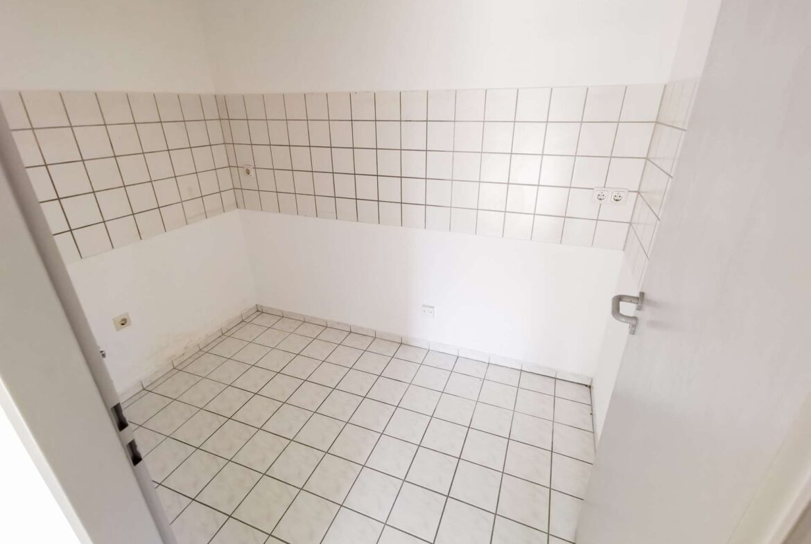 Empty utility room with white square tiles on the walls and floor, and a door visible on the right.