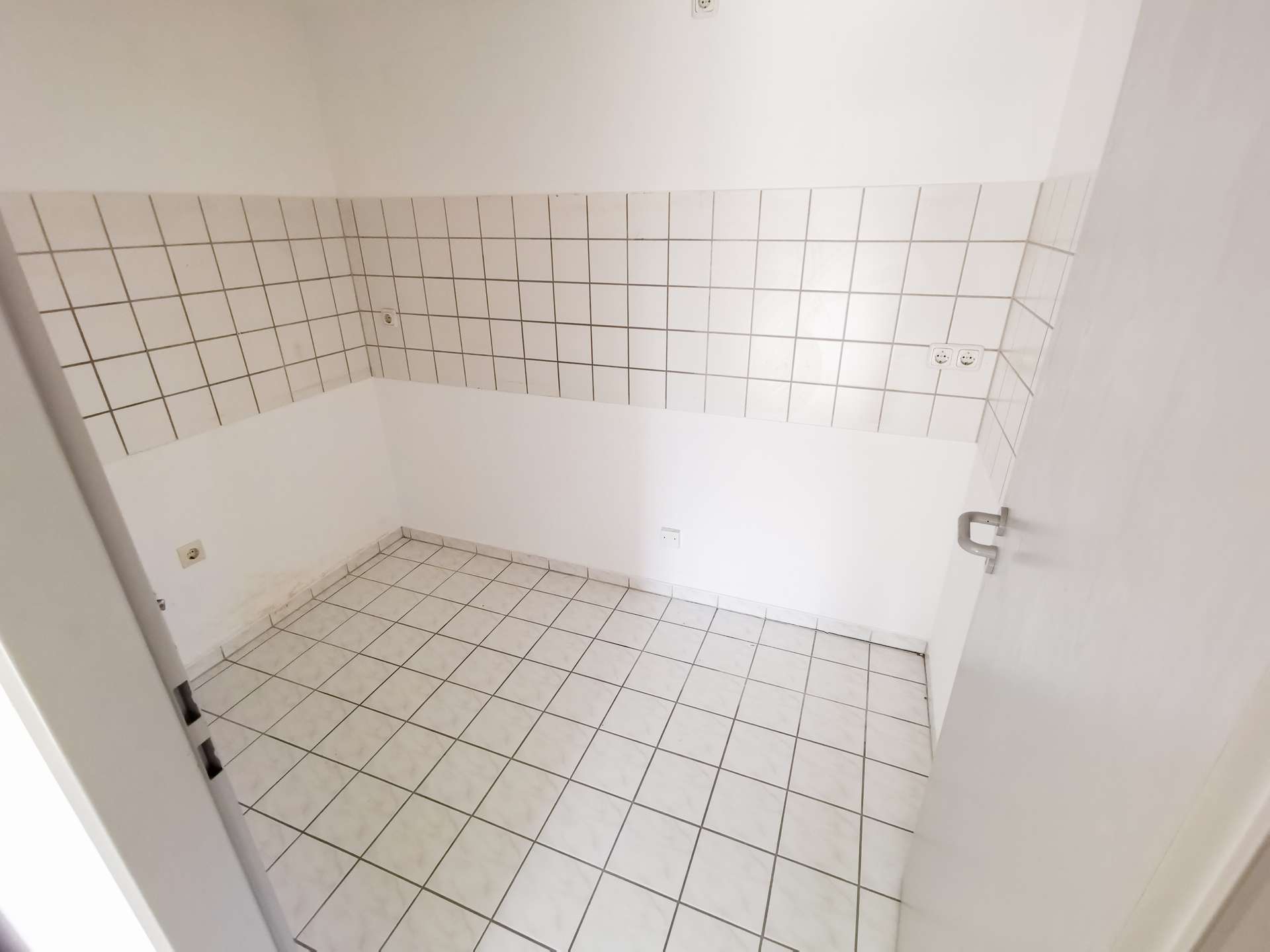 Empty utility room with white square tiles on the walls and floor, and a door visible on the right.