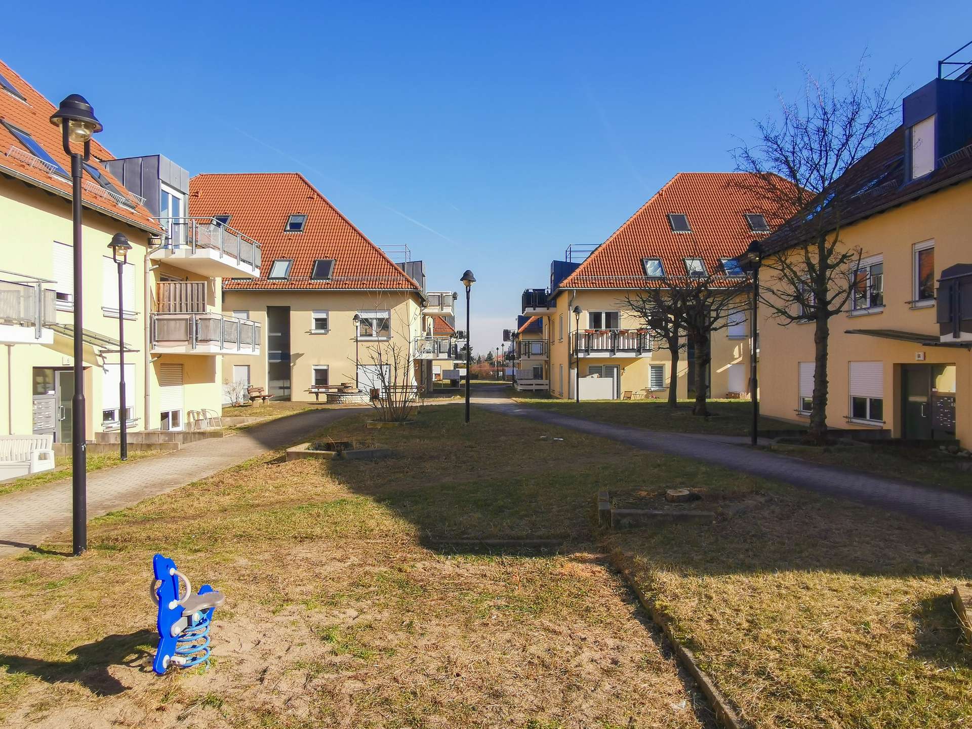 Residential courtyard with yellow apartment buildings, red-tiled roofs, and a blue spring rider in the foreground.