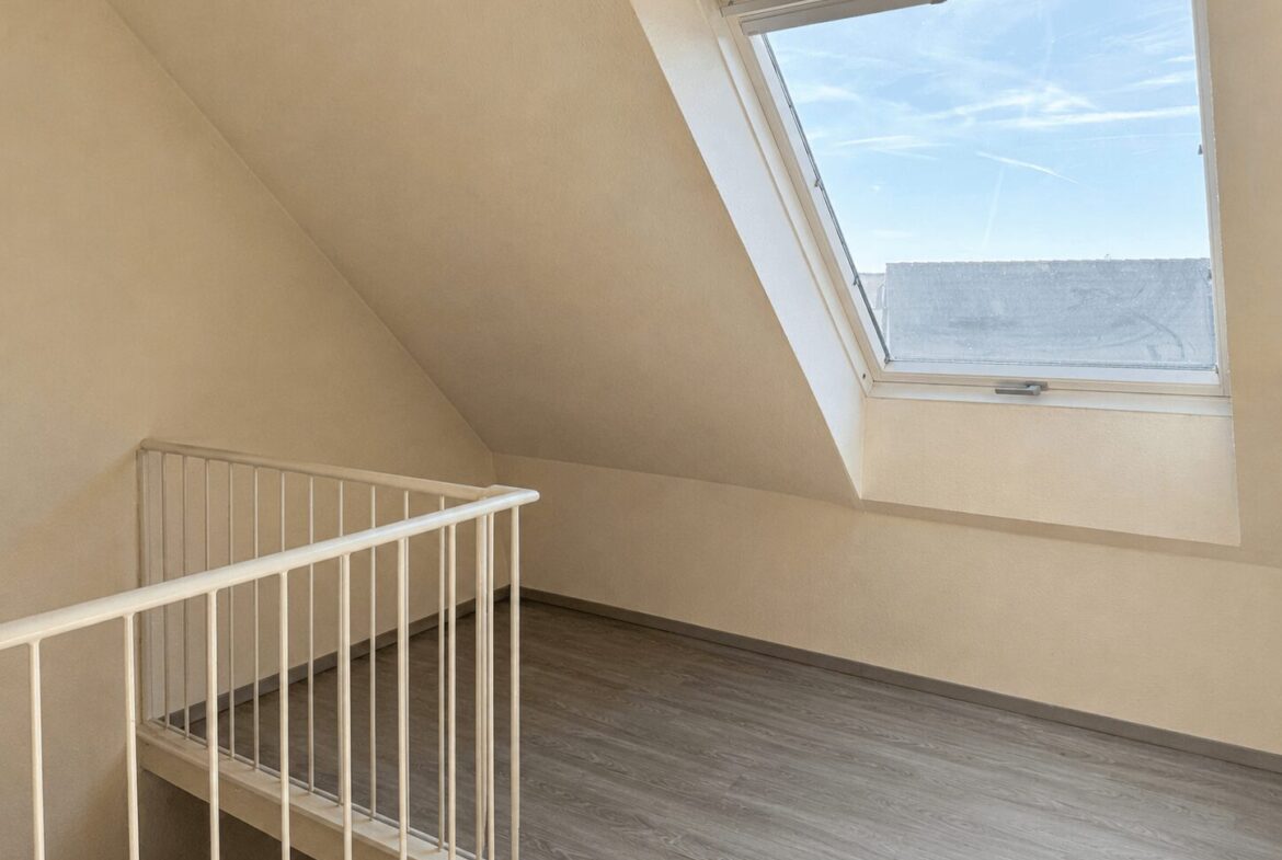 Bright empty attic loft with a slanted ceiling, white railing, and a large skylight letting in daylight.