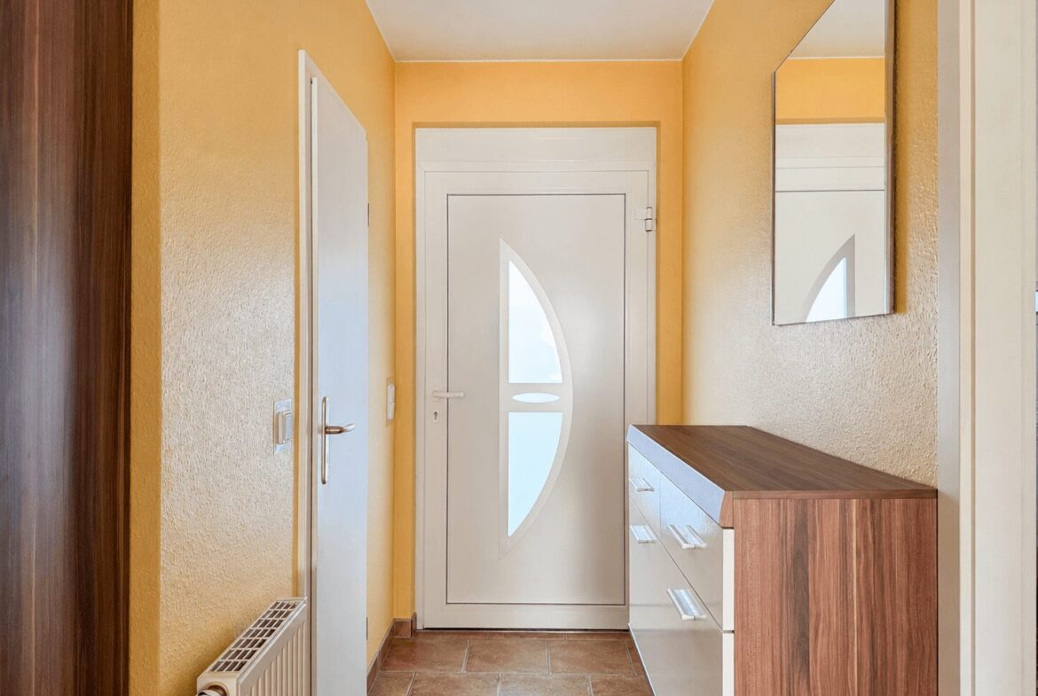 Bright entry hallway with yellow walls, leading to a white front door that has a curved window insert; a wooden-and-white console cabinet is on the right with a wall mirror above.
