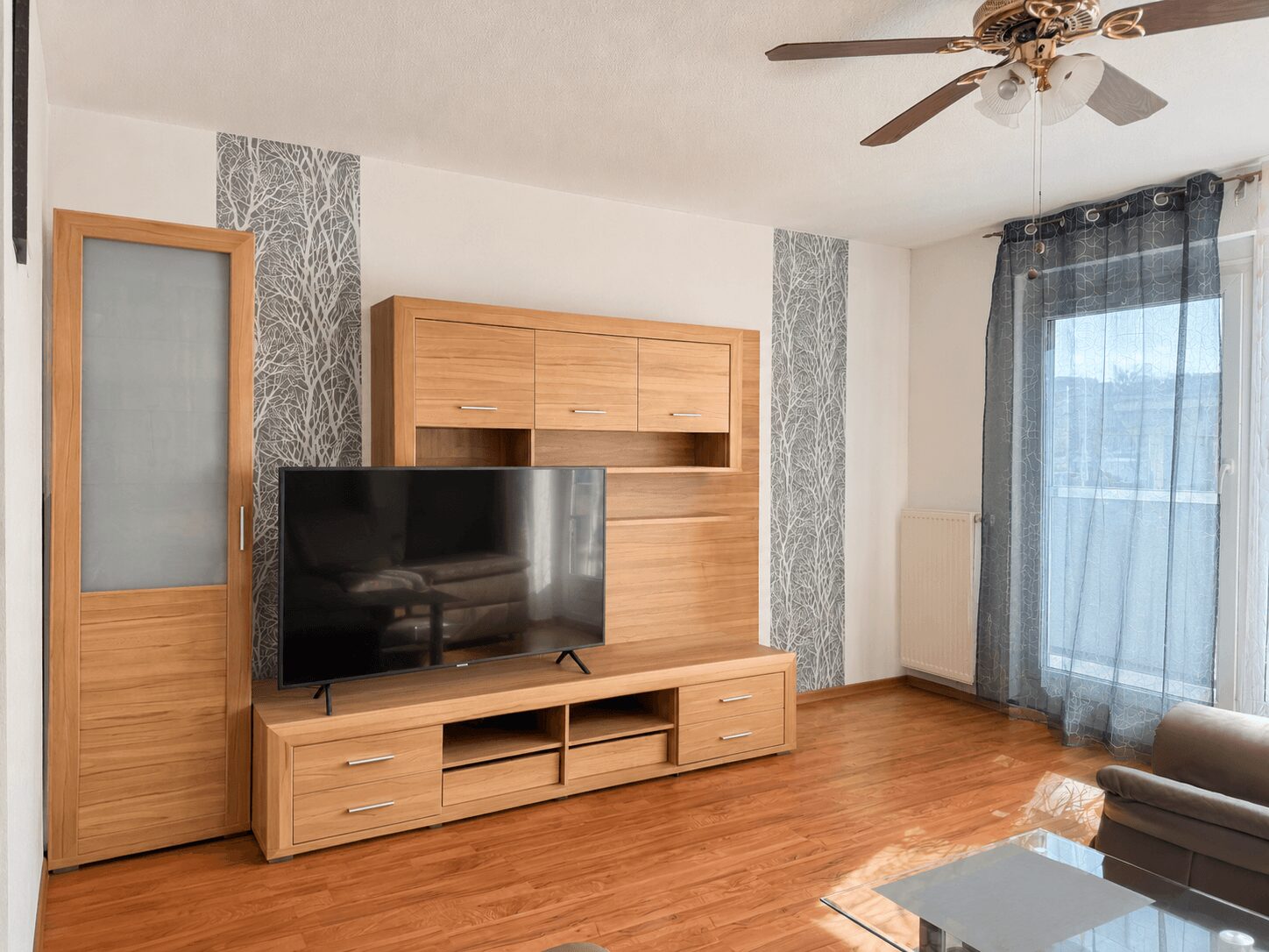 Living room with a wooden entertainment unit, large flat-screen TV on a low cabinet, and hardwood floors.