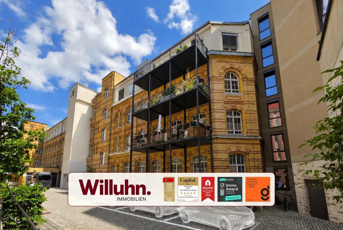 Brick building with black metal balconies advertising Willuhn Immobilien on a white banner in the foreground, blue sky above.