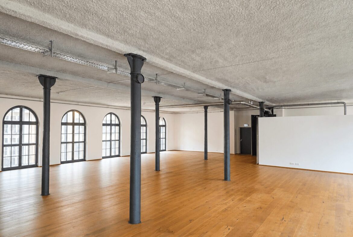 Industrial loft with tall arched windows, black columns, and a warm wooden floor.