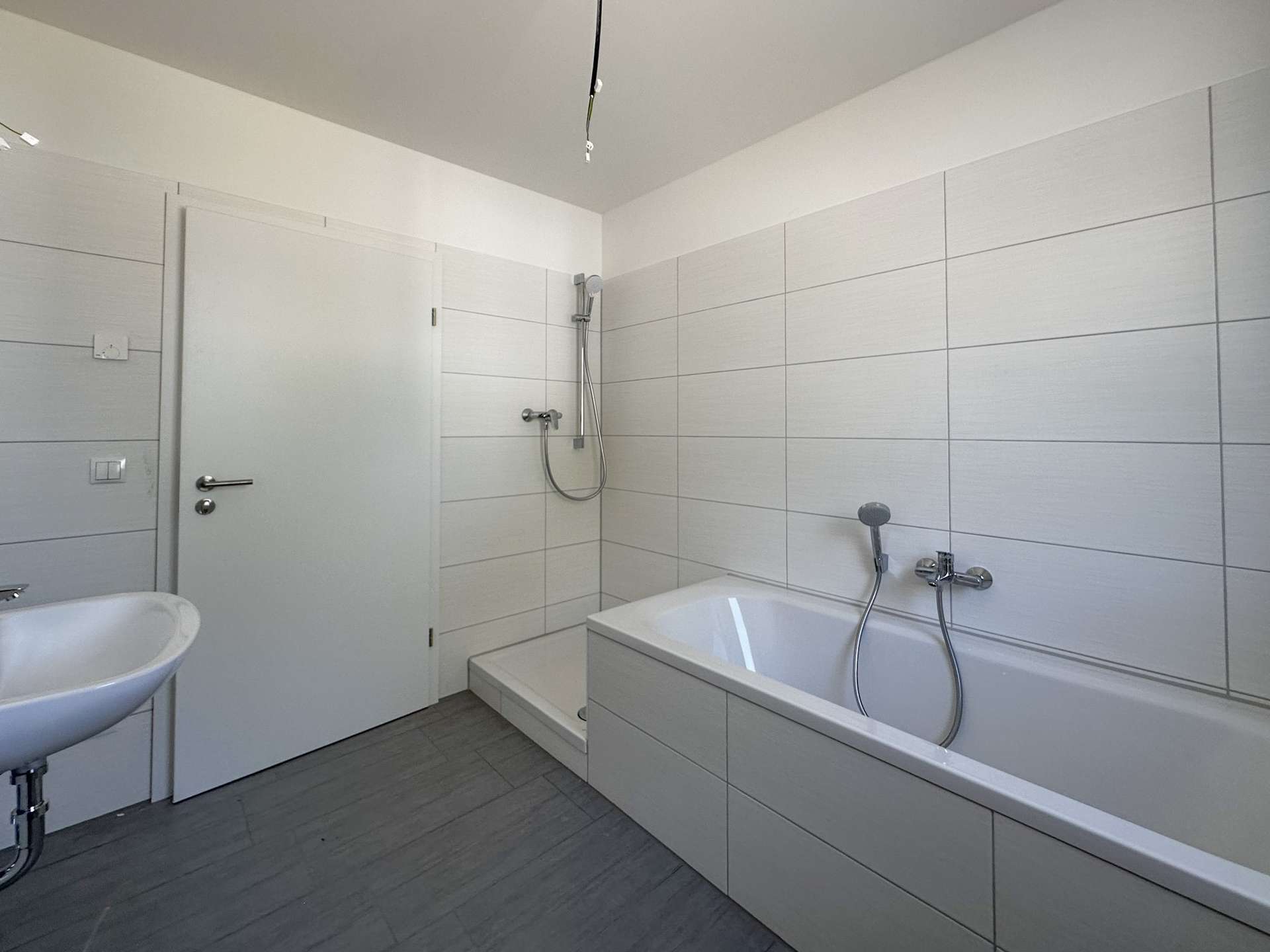 Modern white bathroom with a built-in bathtub, handheld shower, and white sink against tiled walls.