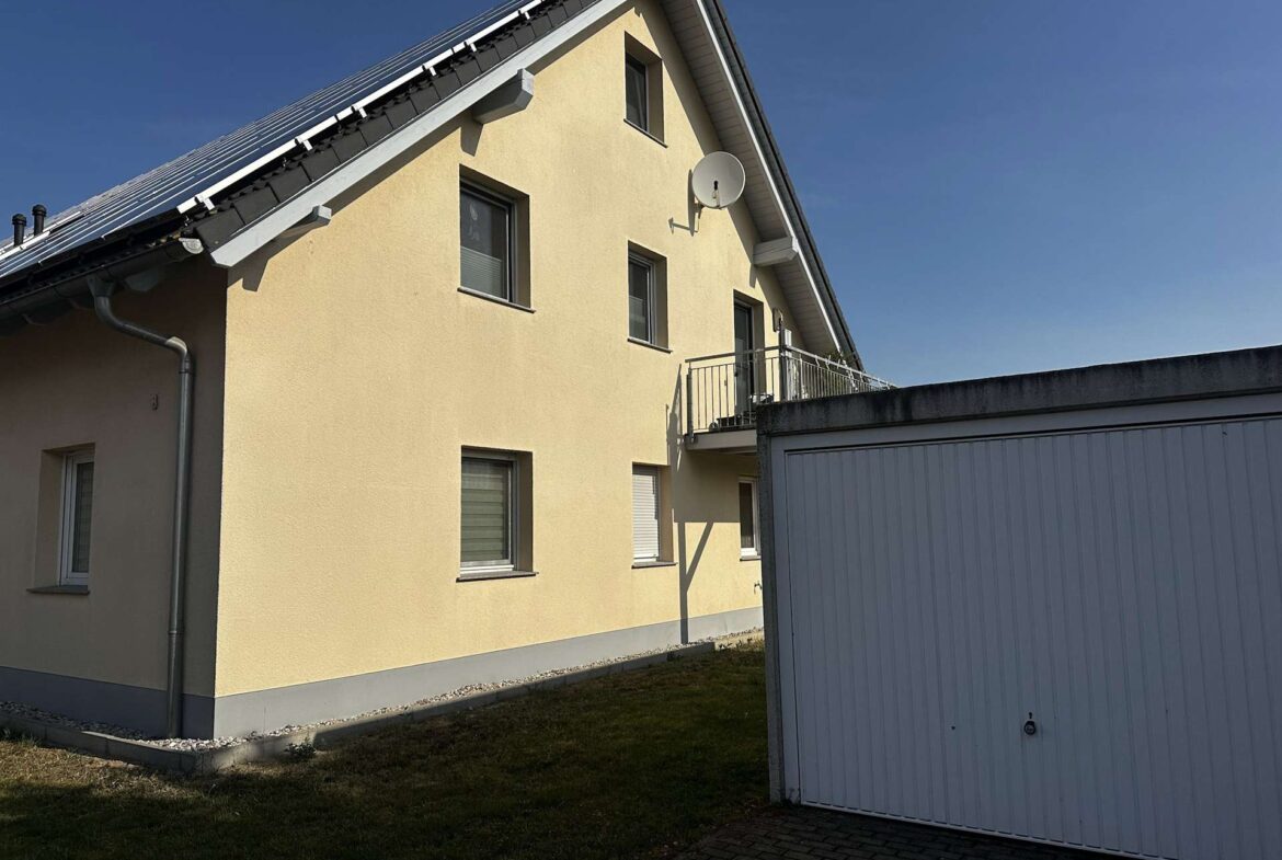 Yellow two-story building with a sloped roof and a satellite dish mounted on the exterior wall, adjacent to a gray garage door against a clear blue sky.