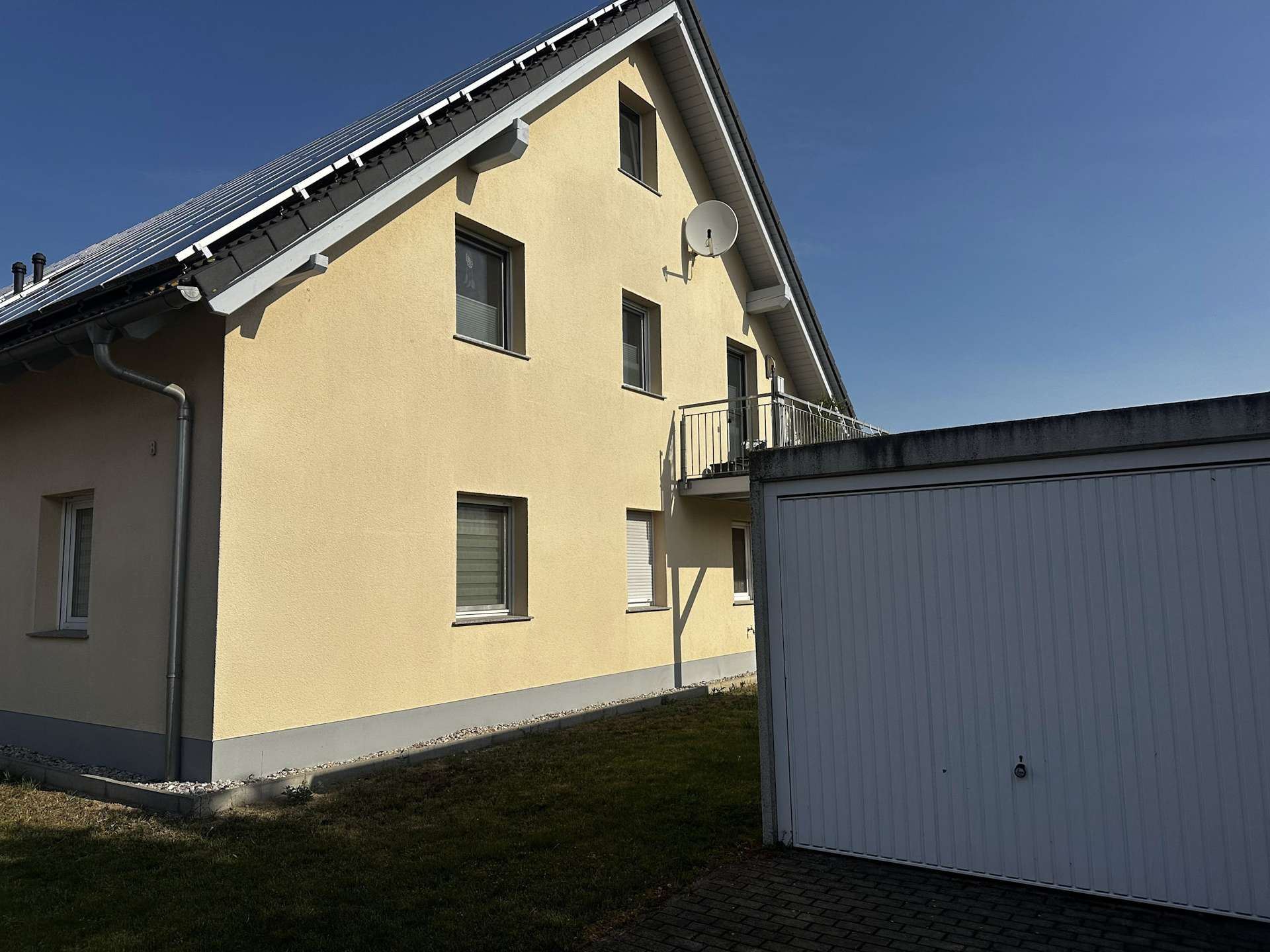Yellow two-story building with a sloped roof and a satellite dish mounted on the exterior wall, adjacent to a gray garage door against a clear blue sky.