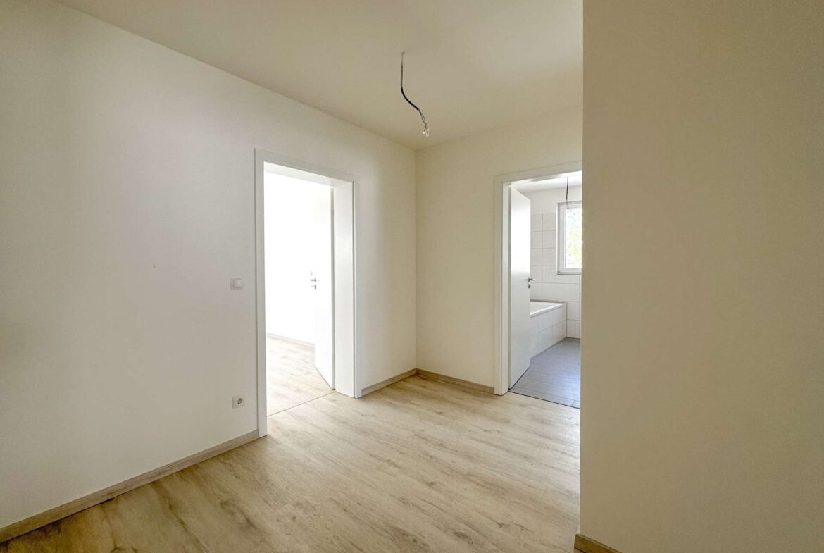 Empty hallway in a light-colored room with open doorways and exposed hanging wires from the ceiling, suggesting unfinished electrical work.