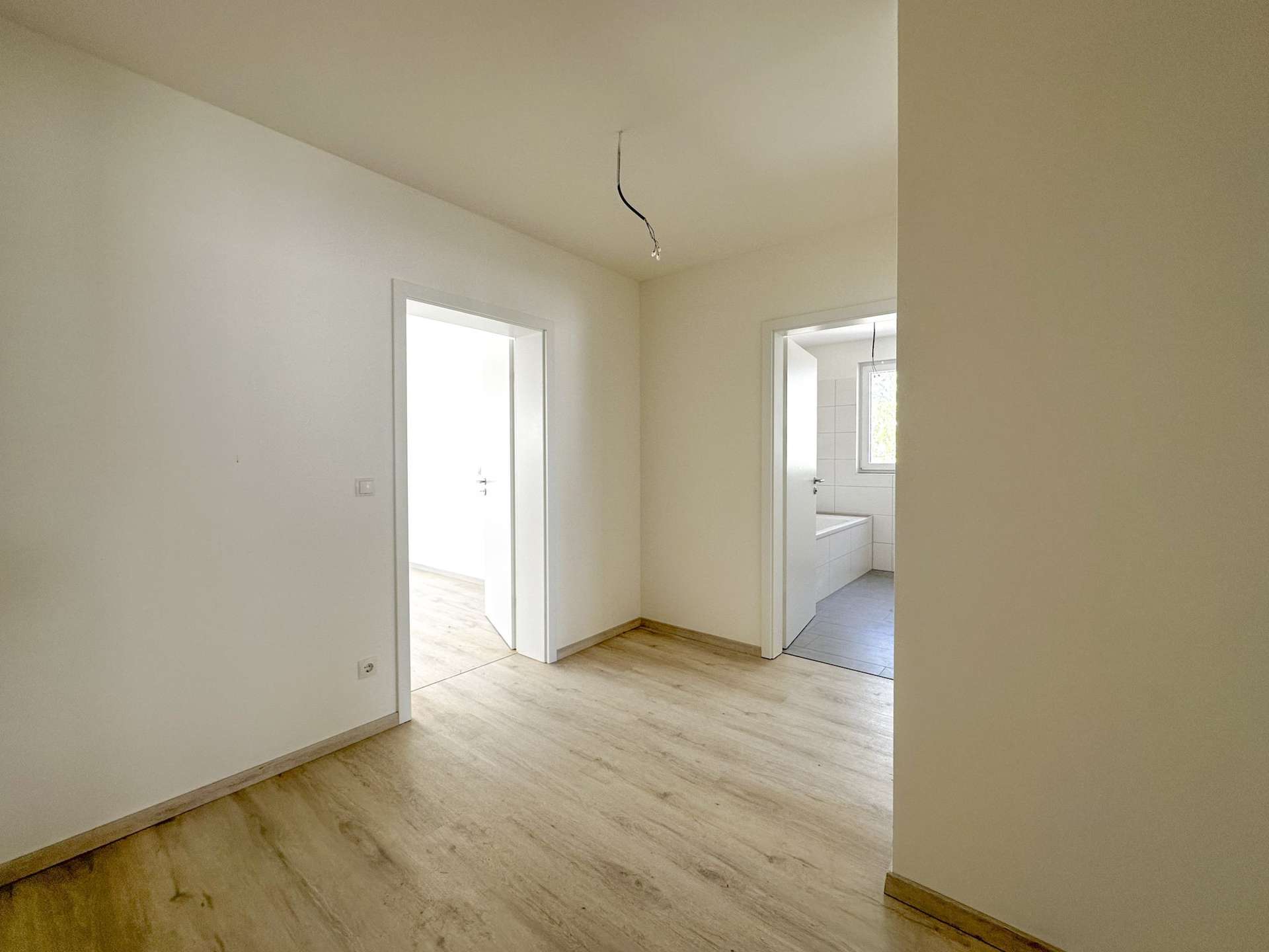 Empty hallway in a light-colored room with open doorways and exposed hanging wires from the ceiling, suggesting unfinished electrical work.
