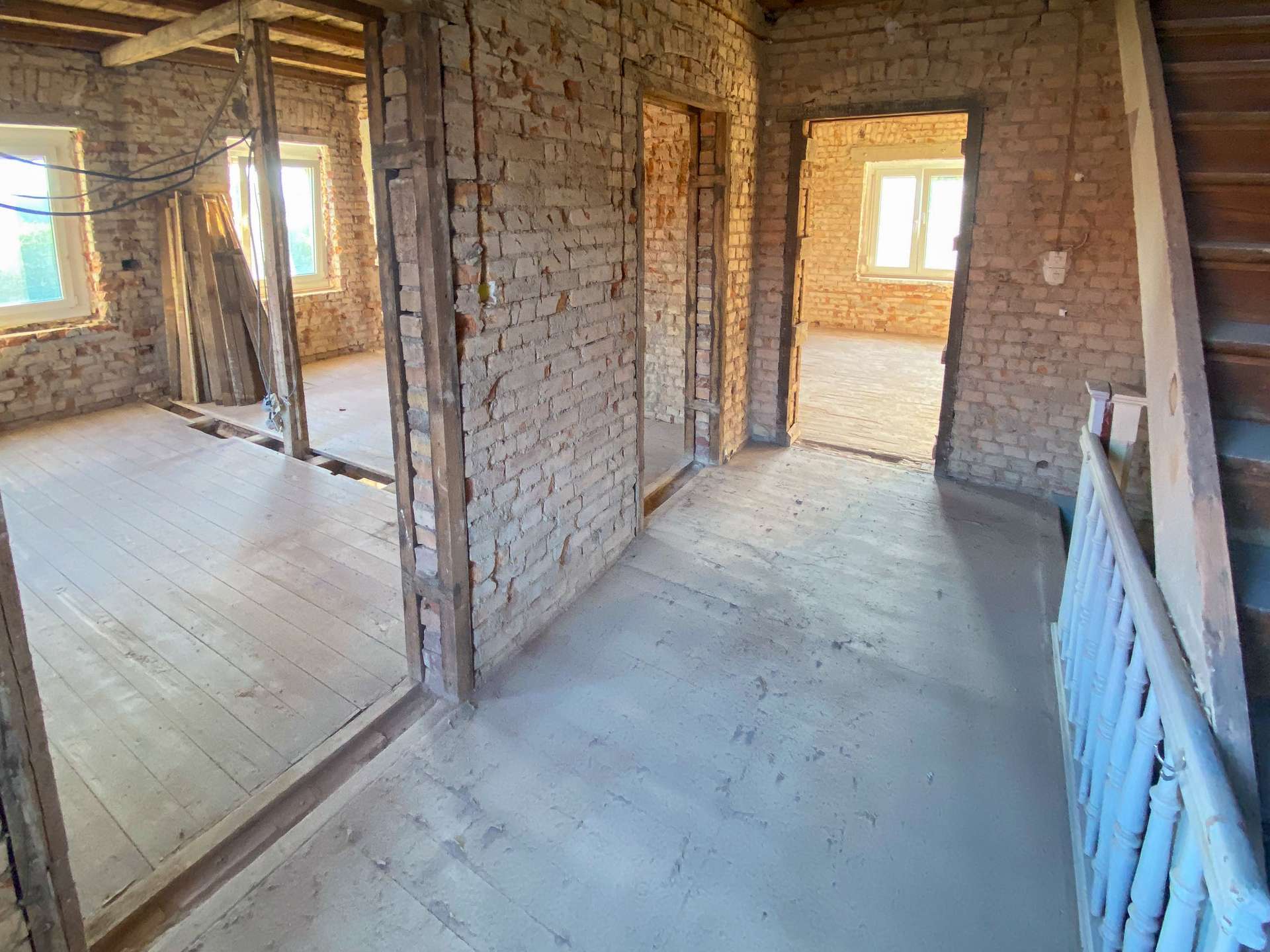 Interior of a brick-walled construction site with exposed beams and a doorway leading to a sunlit room.