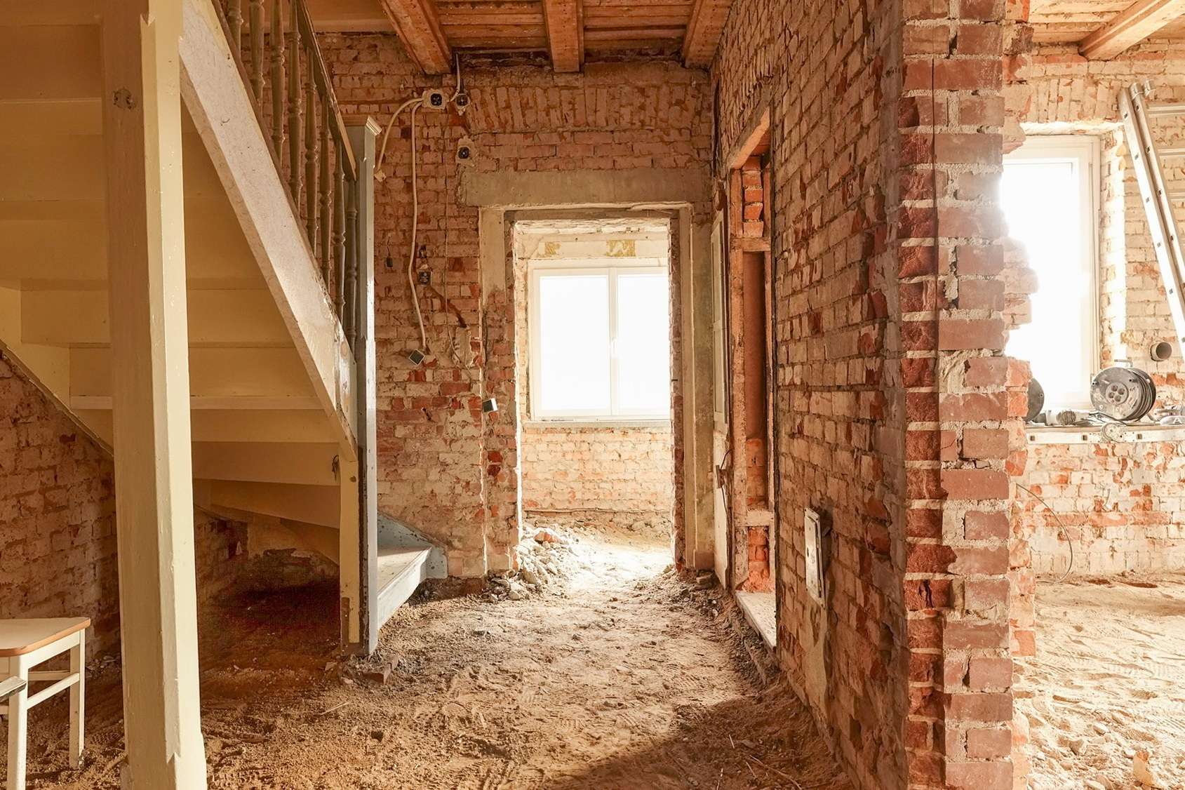 Interior of a brick-walled renovation site with a wooden staircase on the left and exposed wiring