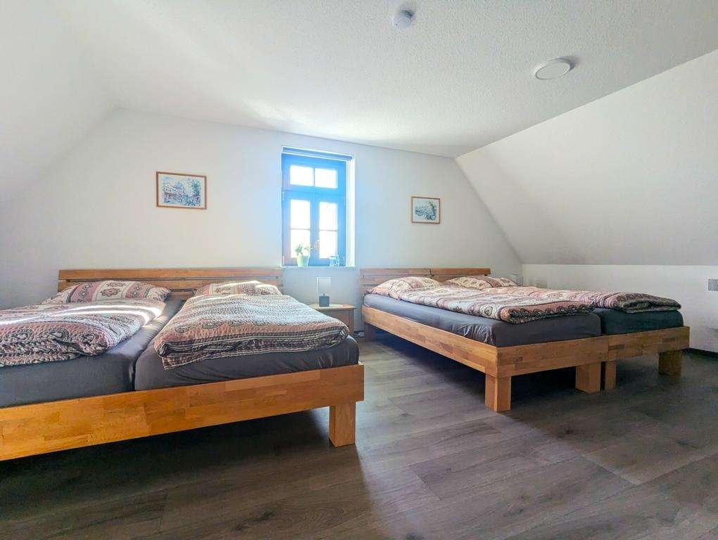 Attic bedroom with two wooden twin beds, patterned quilts, and a window between them.
