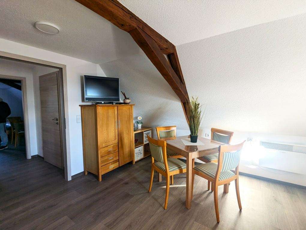 Dining area under a sloped ceiling with a wooden table, four striped chairs, and a TV on a cabinet.