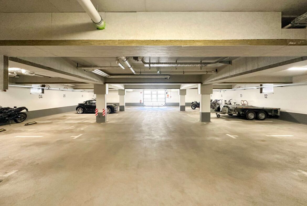 Underground parking garage with concrete pillars, parked cars along the sides, and a trailer on the right edge of the image.