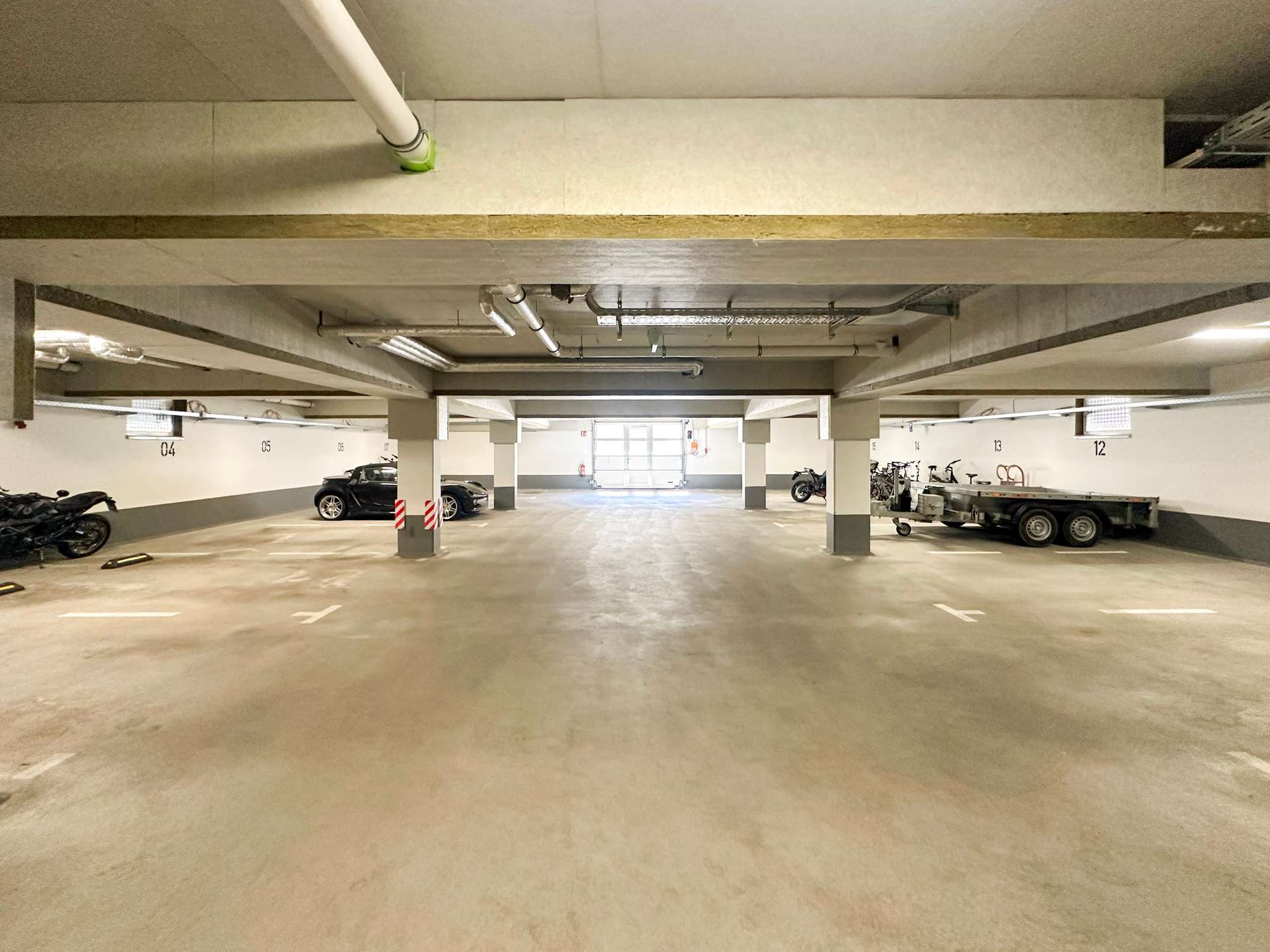 Underground parking garage with concrete pillars, parked cars along the sides, and a trailer on the right edge of the image.