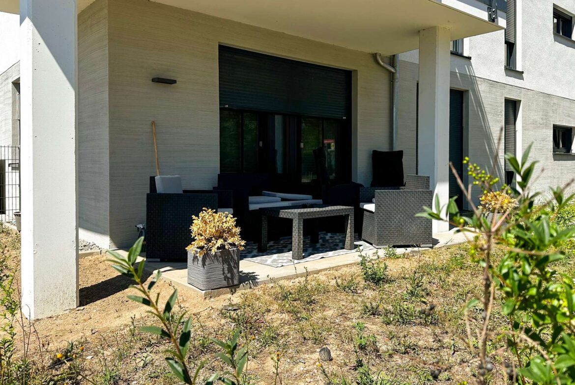 Modern patio seating area outside a beige stucco house, featuring black wicker furniture and potted plants.
