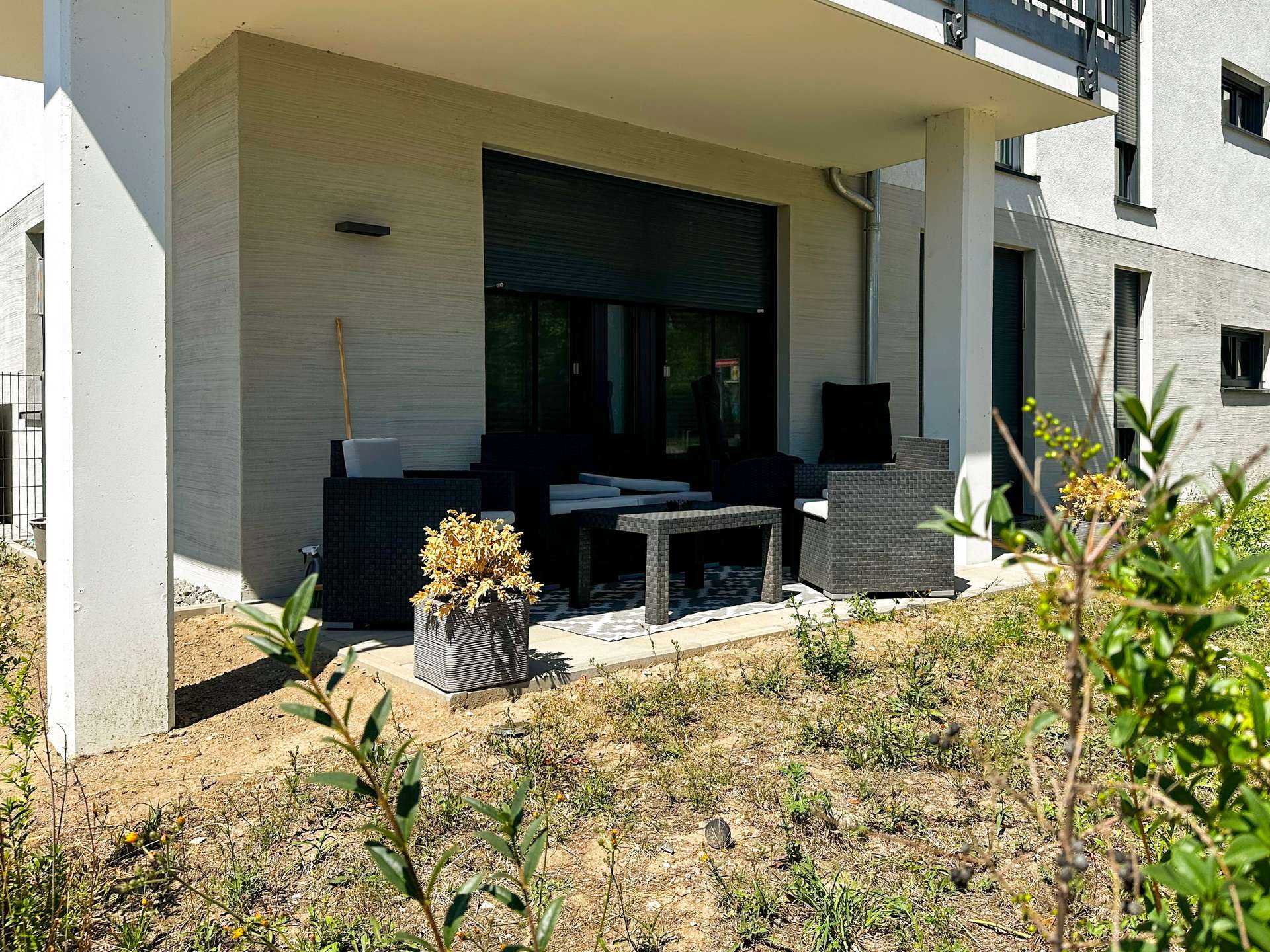 Modern patio seating area outside a beige stucco house, featuring black wicker furniture and potted plants.