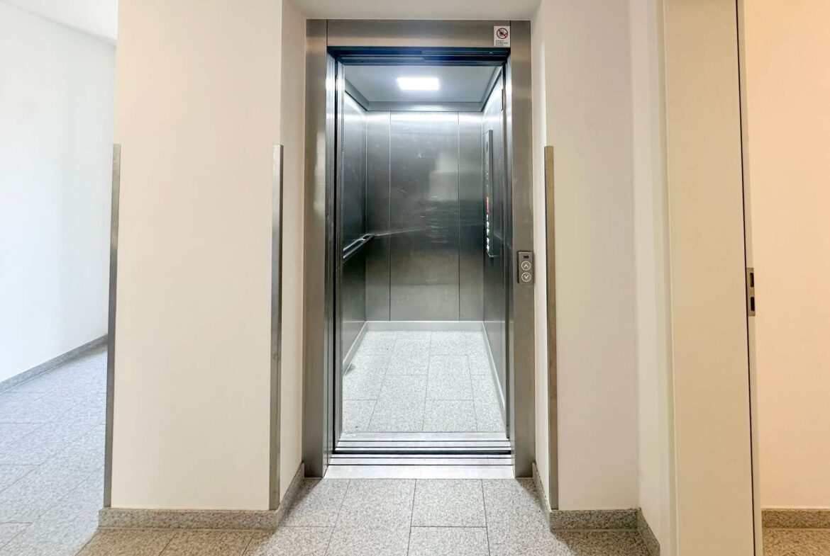 Open elevator with stainless steel interior in a beige-walled hallway to the right.